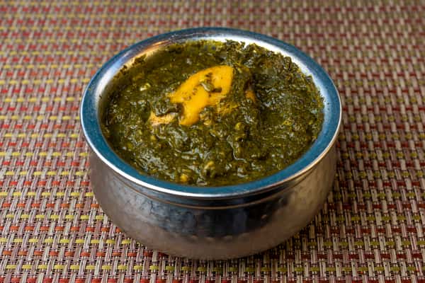 Saag chicken in a thick spinach gravy served in a traditional metal bowl — classic North Indian curry with tender chicken and greens.