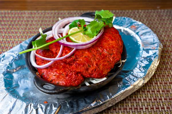 Tandoori chicken served on a sizzling skillet with onion rings, cilantro, and lemon slices — classic Indian clay oven chicken.