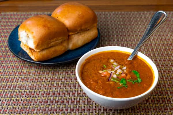 Pav bhaji served with buttered bread rolls and a bowl of spiced vegetable mash, garnished with chopped onions and cilantro.