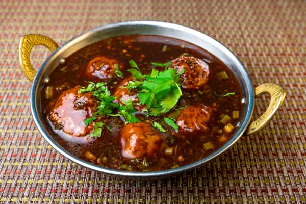 Veg Manchurian — crispy vegetable dumplings in a savory Indo-Chinese soy garlic gravy, garnished with fresh cilantro.