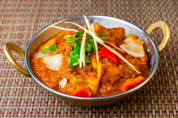 Spicy Indo-Chinese chili chicken with bell peppers, onions, and cilantro in a savory brown sauce, served in a metal karahi dish.