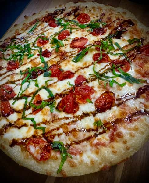 Margherita-style pizza from Elberta Pizza in Elberta, AL with melted mozzarella, roasted cherry tomatoes, fresh basil, and balsamic drizzle.