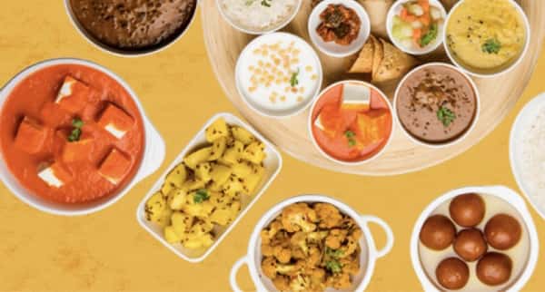 Traditional Indian thali spread with paneer curry, dal, rice, assorted vegetables, and gulab jamun, displayed in a colorful, authentic meal arrangement.