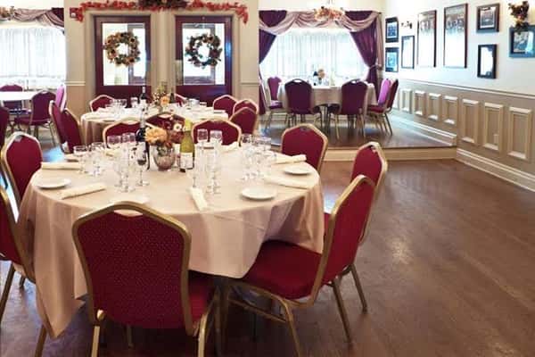 tables in a catering hall with a white tablecloth and 8 chairs and place settings per table