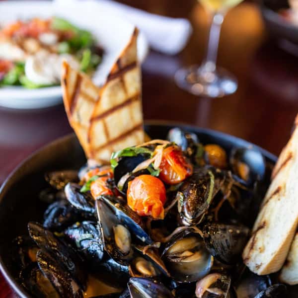 Steamed mussels with cherry tomatoes, herbs, and garlic served in broth with grilled artisan bread.