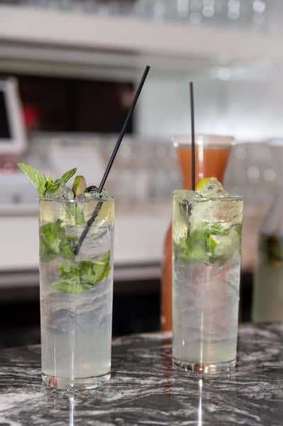 Two mojito cocktails with mint leaves and lime, served over ice in tall glasses, resting on a marble bar counter.