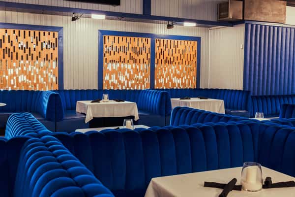 A cozy dining area with plush blue velvet booths and modern wooden panel walls, complemented by clean white tables with candle holders.