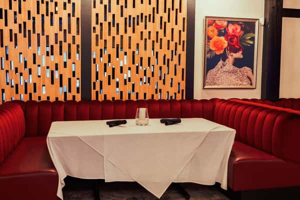 A cozy restaurant booth with red velvet seating, a white tablecloth, and an artistic floral portrait on the wall.