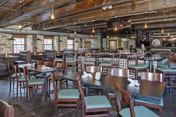 spacious restaurant dining room with wooden tables, exposed beams, and open bar seating