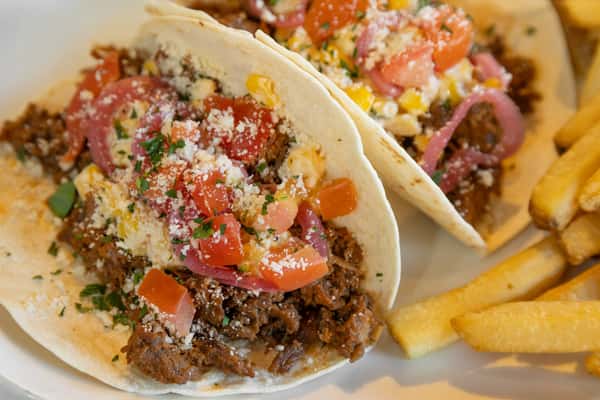 close-up of barbacoa tacos with fresh salsa, shredded cheese, and seasoned fries