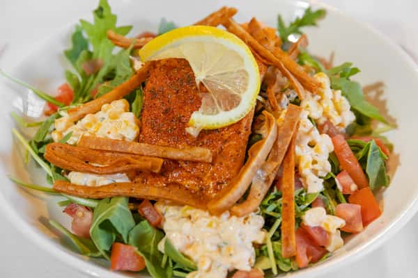 crispy salmon salad with street corn, mixed greens, and fresh vegetables served with lemon