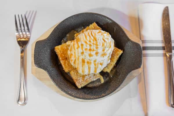warm cornbread dessert topped with whipped cream and caramel drizzle in a skillet