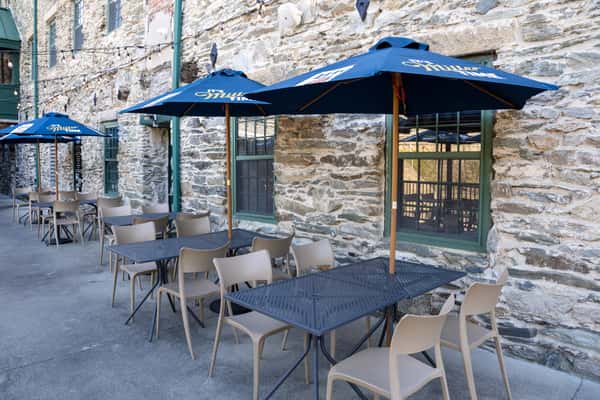 stone patio dining area with blue umbrellas and outdoor seating beside a rustic restaurant exterior