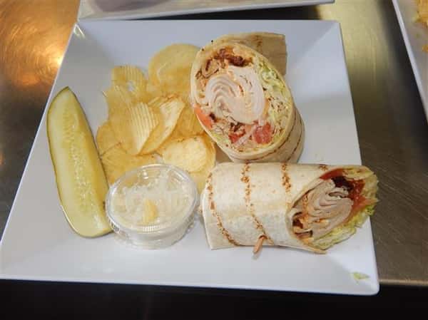 turkey club wrap with bacon and a side of chips with coleslaw and a pickle spear