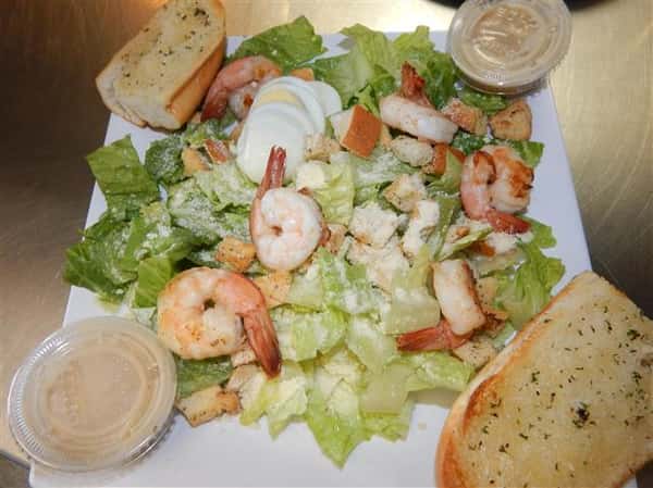 salad topped with cooked shrimp, eggs and croutons with garlic bread on the side
