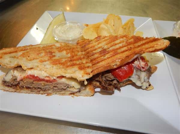 roast beef panini with cheese and peppers with a side of chips, coleslaw and a pickle spear