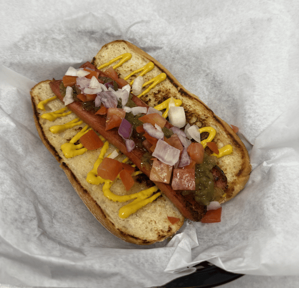Grilled hot dog topped with diced tomatoes, onions, relish, and mustard in a toasted bun.