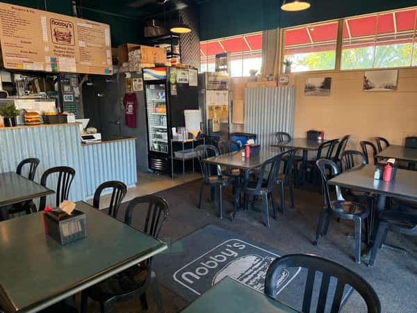 Casual diner interior at Nobby's with black chairs, simple tables, order counter, and a menu board above.