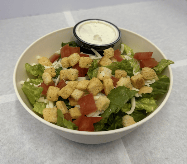 A fresh salad with lettuce, tomatoes, shredded cheese, and croutons, served with a side of ranch dressing.