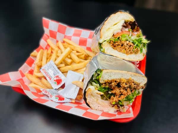 Philly cheesesteak sub cut in half with crinkle-cut fries and ketchup packets in a red basket.