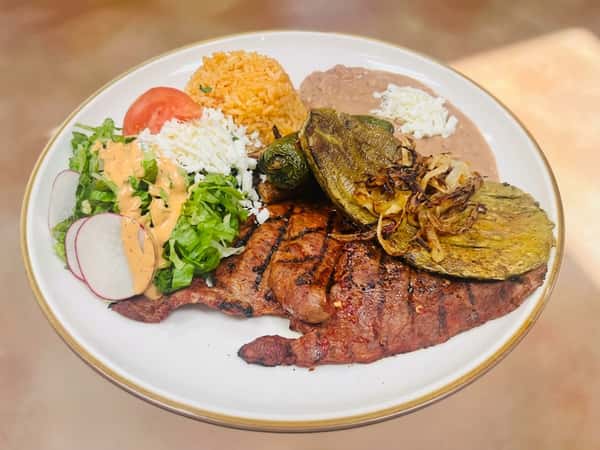 Grilled steak with nopales, calabacitas, rice, refried beans, and a side salad on a white plate.