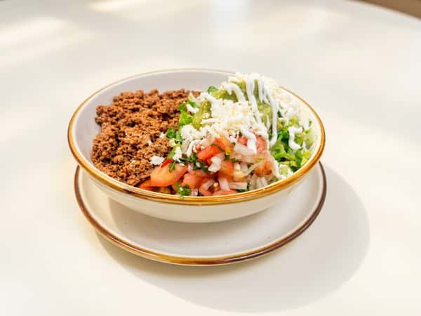 Taco bowl with ground beef, pico de gallo, guacamole, shredded lettuce, cheese, and crema.
