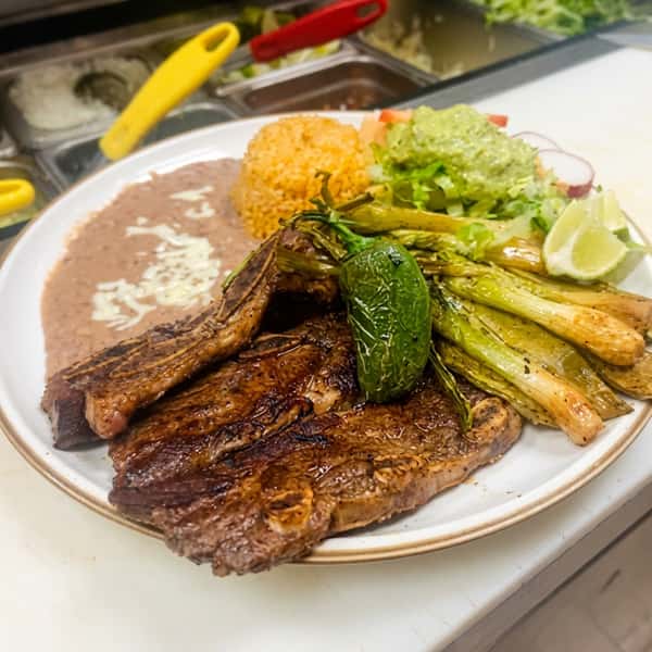 Grilled steak with refried beans, rice, grilled green onions, and a jalapeño.