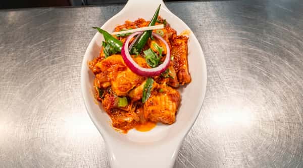 Spicy chilli chicken pieces garnished with sliced red onion, fresh chillies and colourful peppers.