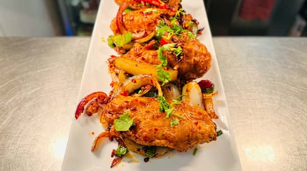 Stack of spicy grilled chicken wings coated in a vibrant marinade and garnished with fresh herbs.