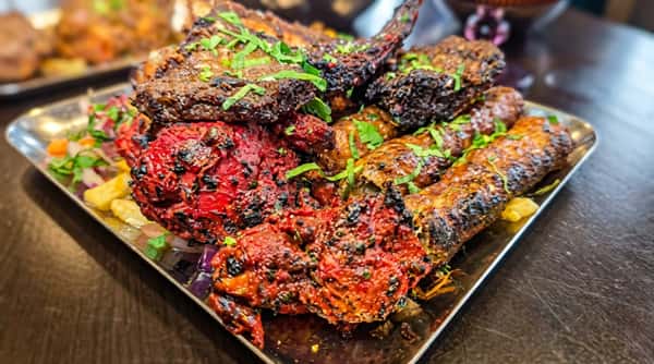 Colourful mixed grill platter featuring chargrilled meats coated in aromatic spices and garnished with fresh herbs.