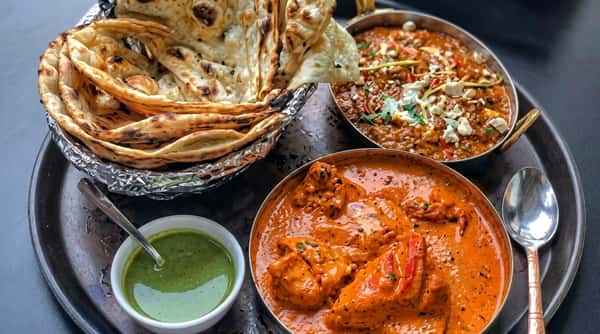 Rich chicken tikka masala served alongside freshly baked naan bread and a bowl of green chutney.