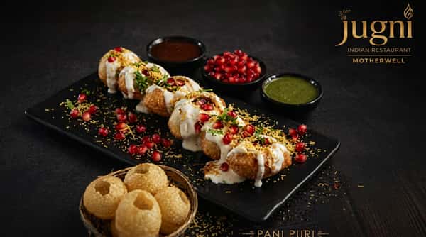 Pani puri arranged on a dark platter with colourful garnishes and a selection of vibrant dipping sauces.