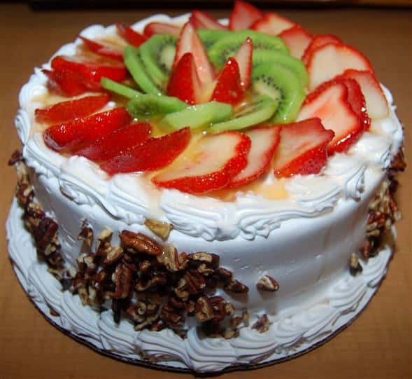 cake with icing topped with sliced fruit and chopped nuts on the side