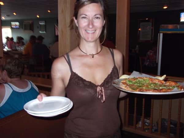 Woman holding plates and a pizza and smiling for photo