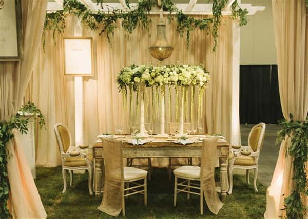 white trellis with vines hanging above a table with a white floral centerpiece with more vines