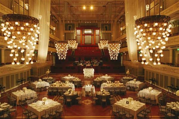 overview of catering room with chandeliers, red wood floors, large white tables