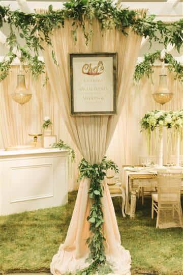 a white table with white floral centerpiece with green vines hanging