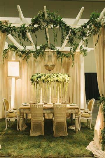a white table with white floral centerpiece with green vines hanging