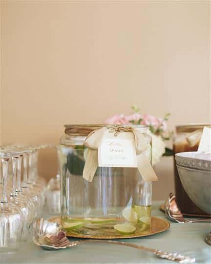 big jars of cucumber water with wine glasses next to it