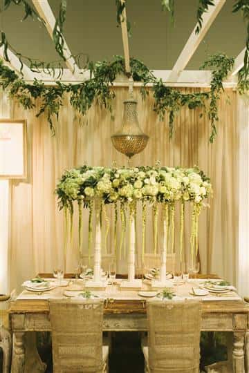 a white table with white floral centerpiece with green vines hanging