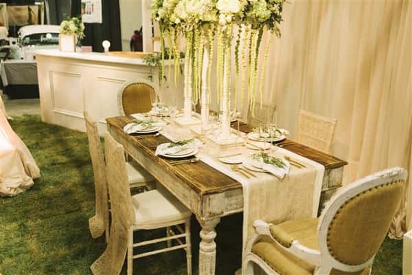 a white table with white floral centerpiece with green vines hanging