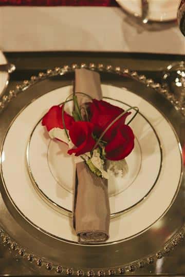 white plate with brown napkin with utensils rolled up with red roses on top
