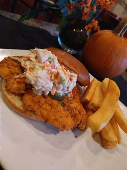 Fried chicken sandwich topped with coleslaw, served with thick-cut fries on a white plate.