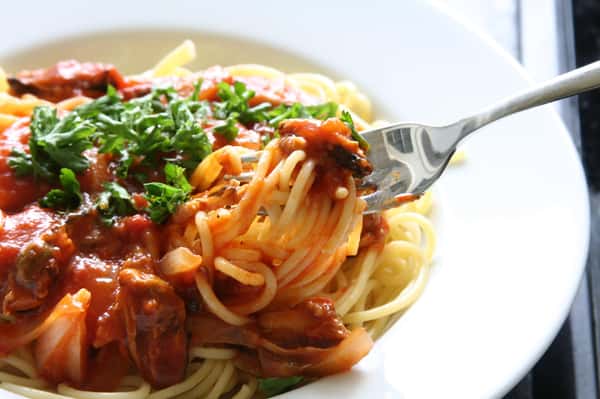 Spaghetti topped with rich tomato sauce, sautéed vegetables, and fresh parsley, twirled on a fork ready to eat.