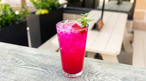 Bright pink dragon fruit mojito with fresh mint and ice served in a tall glass on an outdoor patio table.