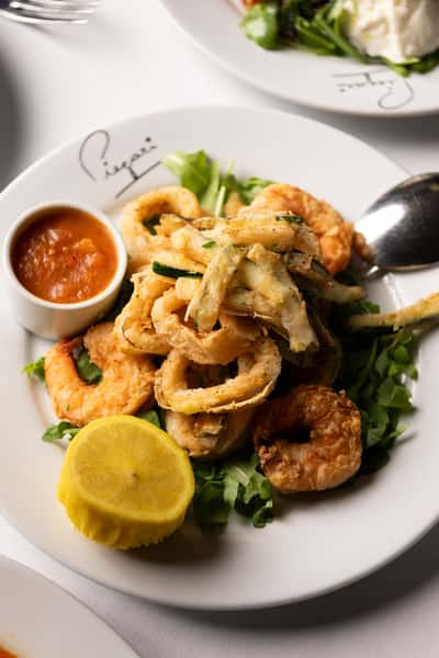 Fried calamari, shrimp, and zucchini on arugula with a lemon slice and marinara dipping sauce on a white plate.