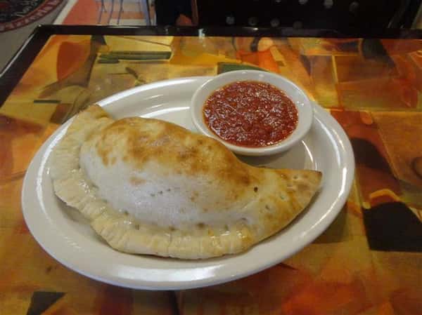 baked calzone on a plate with a bowl of tomato dipping sauce