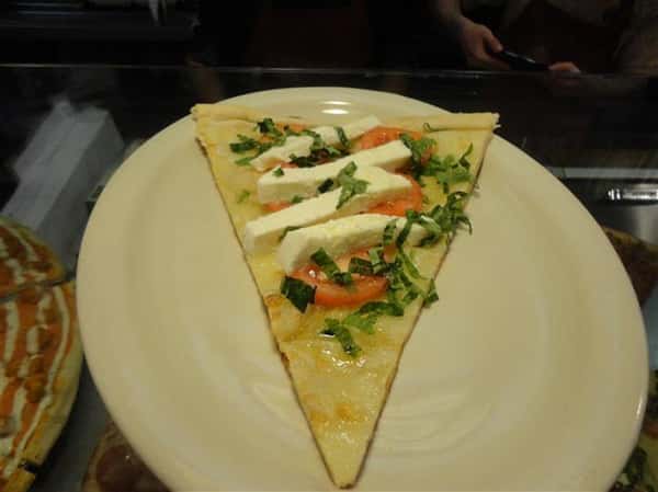 single slice of pizza on a plate with cheese, tomatoes, lettuce and mozzarella
