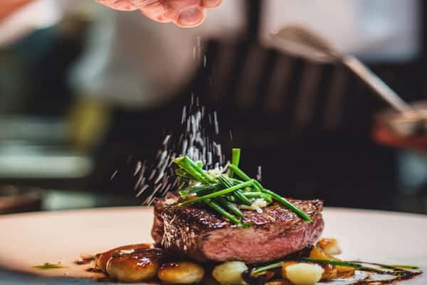 Steak being seasoned with salt