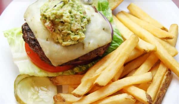 cheeseburger topped with guacamole with lettuce and tomato and french fries on the side
